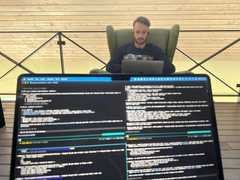 Muž v zeleném ušáku s notebookem, v popředí velká obrazovka s otevřeným terminálem